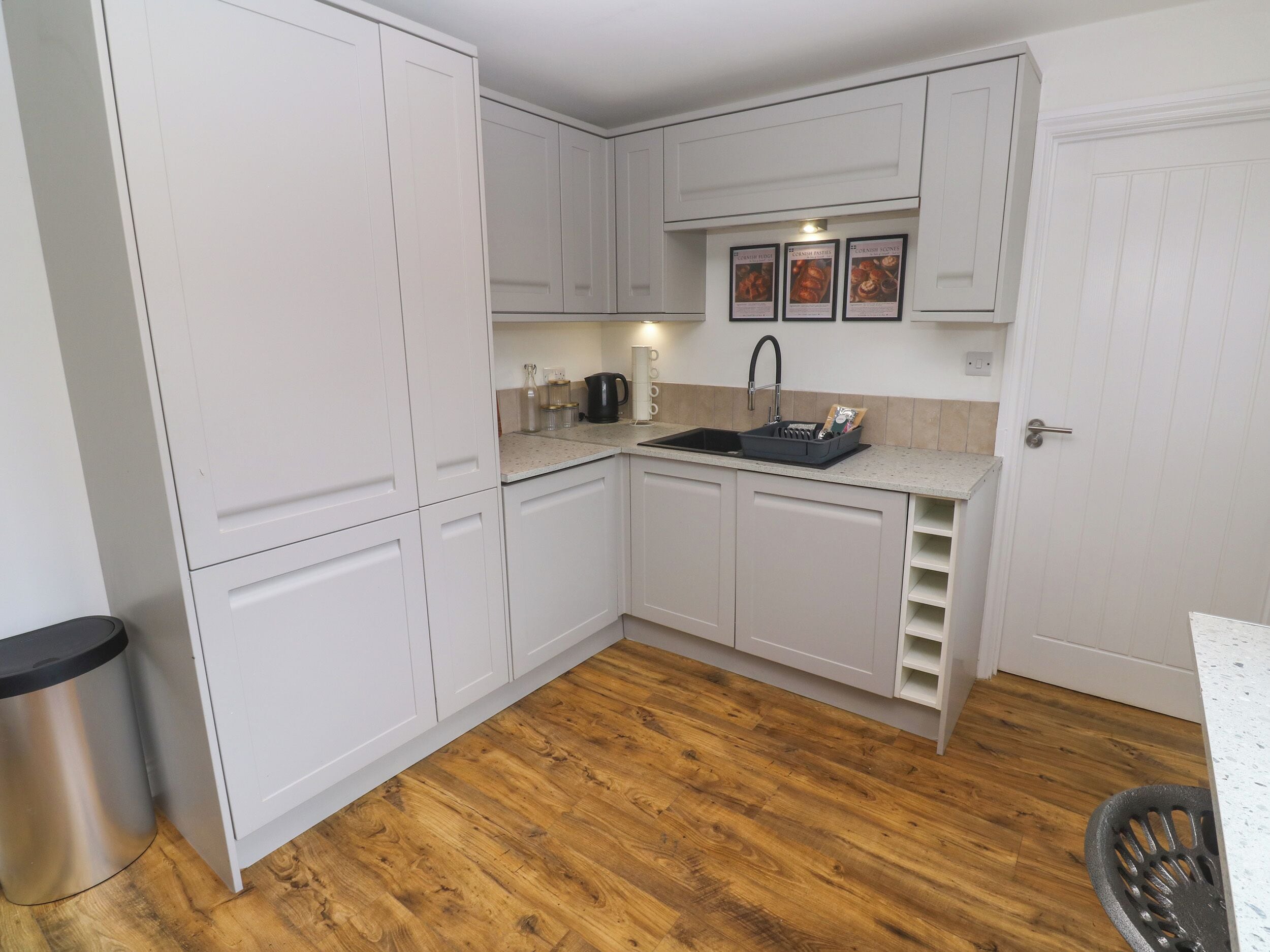 Cocina compacta con armarios blancos, un bote de basura de acero inoxidable y piso de madera.