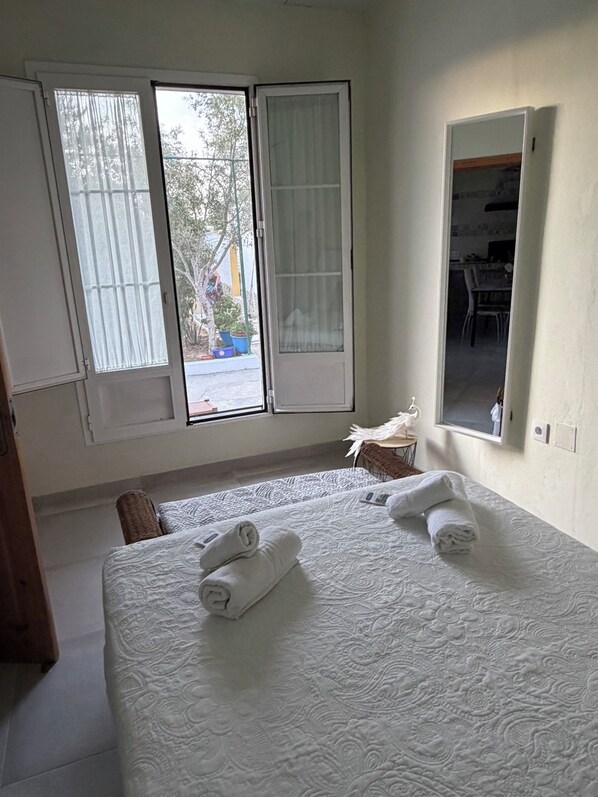 A hotel room with a large bed, two windows, a small table, and a chair.