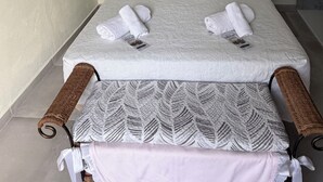 Un lit simple avec une tête de lit blanche, deux oreillers et deux serviettes enroulées.