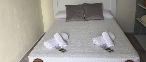 A single bed with a white headboard, two pillows, and two rolled towels.