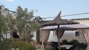Un espace patio doté d’un toit de chaume, de mobilier d’extérieur et d’un petit jardin.