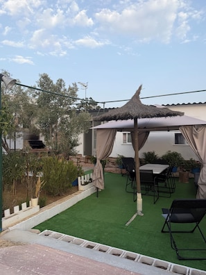Un espace patio doté d’un toit de chaume, de mobilier d’extérieur et d’un petit jardin.