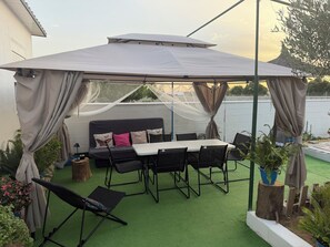 An outdoor patio with a covered seating area, a table, and chairs.