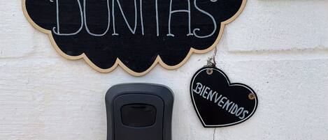 Un letrero en la pared con 'LAS DUNTAS' y la etiqueta 'BIENVENIDOS', un portero automático negro y una pared con textura.