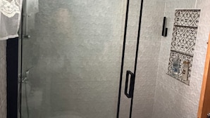 Une douche fermée par des parois de verre, avec un mur recouvert de carreaux et un motif décoratif en carreaux.