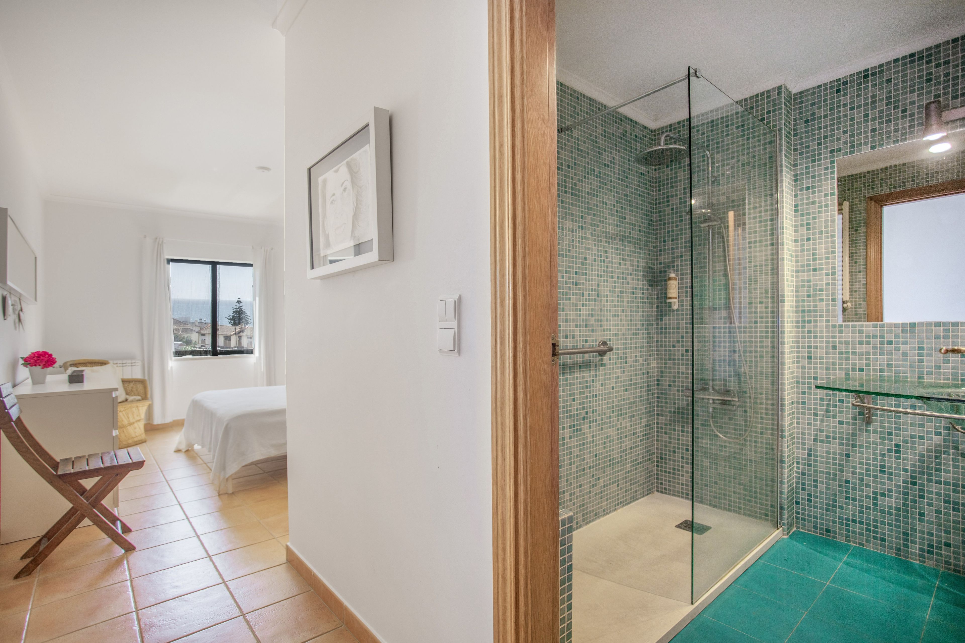 Un baño moderno con cabina de ducha de vidrio, zona de ducha con azulejos verdes y lavamanos con revestimiento de vidrio.