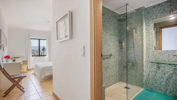 Un baño moderno con cabina de ducha de vidrio, zona de ducha con azulejos verdes y lavamanos con revestimiento de vidrio.