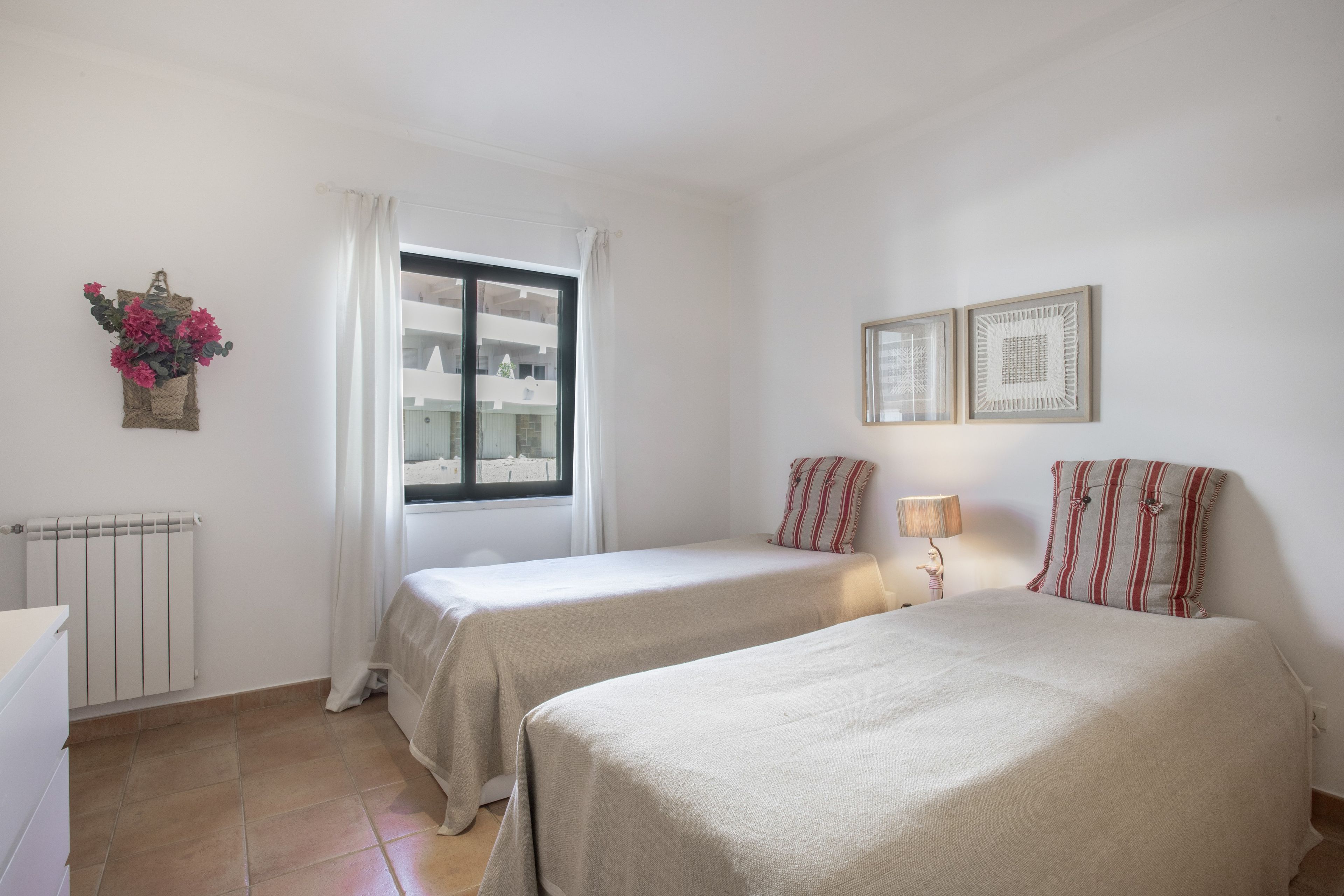 Ein Hotelzimmer mit zwei Betten, einem Fenster mit Vorhängen, einem Heizkörper und einer Wandleuchte.