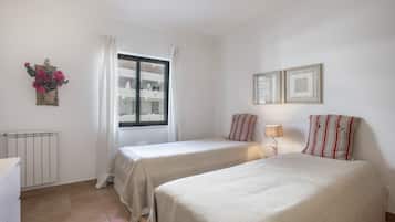 Een hotelkamer met twee bedden, een raam met gordijnen, een radiator en een wandlamp.