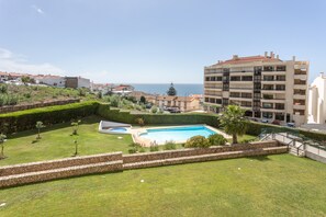Zona residencial amb piscina, vistes al mar i un edifici de diversos pisos al fons.