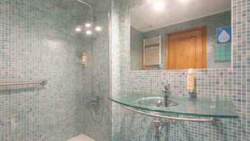 Un baño con lavamanos de vidrio, ducha con mampara de vidrio y puerta de madera.