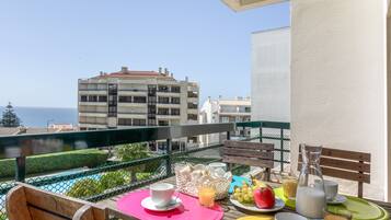 Un balcón con mesa listo para el desayuno, con vista a un edificio y al mar.