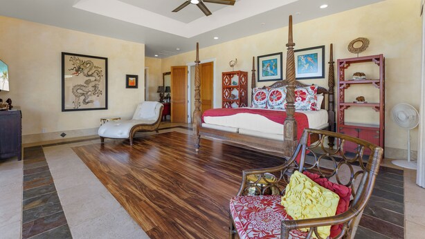 A spacious room with a large bed, a chair, a ceiling fan, and artwork on the walls. - Hula Hula Ranch - 7 Bedrooms, Pool, Ocean View! (Kamuela)