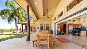 A spacious indoor area with a large dining table, multiple seating options, and a view of a pool and palm trees. - Hula Hula Ranch - 7 Bedrooms, Pool, Ocean View! (Kamuela)