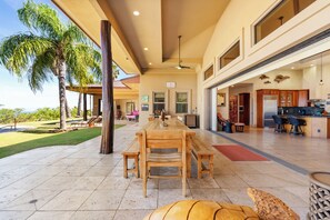 A spacious indoor area with a large dining table, multiple seating options, and a view of a pool and palm trees. - Hula Hula Ranch - 7 Bedrooms, Pool, Ocean View! (Kamuela)