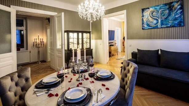 A dining area with a chandelier, a table set for a meal, and a sofa in the background. - Sophies Place Augarten (Wien)
