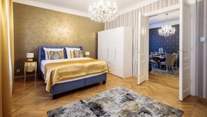 A bedroom with a bed, bedside tables, a chandelier, and a view into a dining area. - Sophies Place Augarten (Wien)