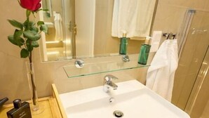 A bathroom with a white sink, a glass-topped vanity, a mirror, and a shower area. - Sophies Place Augarten (Wien)