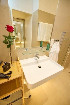A bathroom with a white sink, a glass-topped vanity, a mirror, and a shower area. - Sophies Place Augarten (Wien)