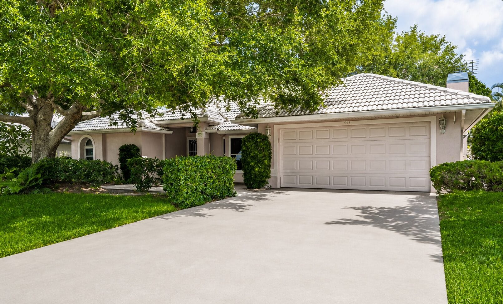 A residential house with a driveway, garage, and a large tree providing shade.