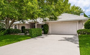 Ein Wohnhaus mit Auffahrt, Garage und einem großen Baum, der Schatten spendet.