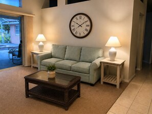 A living room with a green sofa, two side tables with lamps, a coffee table with a plant, and a large wall clock.