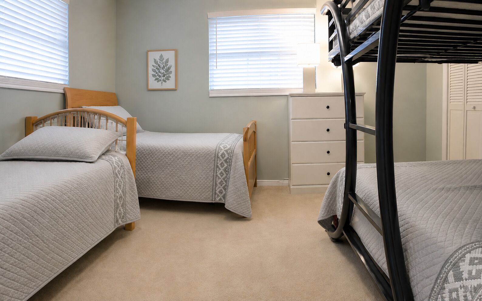 A bedroom with two single beds, a bunk bed, a dresser, and a wall-mounted lamp.