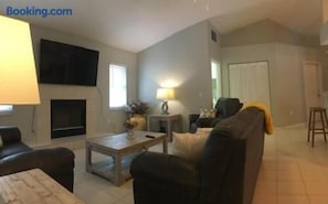 Ein Wohnzimmer mit einer Couch, einem Couchtisch und einem an der Wand befestigten Flachbildfernseher.