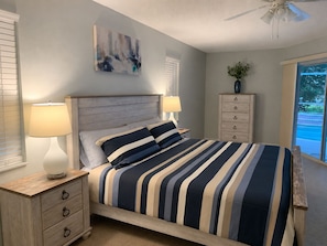 Ein Schlafzimmer mit Bett, Nachttischlampen, einem Schminktisch, einem Deckenventilator, einem Fenster und einem Bild an der Wand.