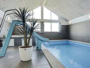 Ein Hallenbad mit blauer Rutsche, einer Kübelpalme und einem gefliesten Boden.