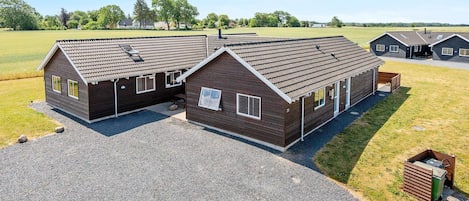 A two-story building with a sloped roof, a gravel driveway, and a grassy field in the background.