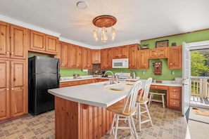 A kitchen with wooden cabinets, a black refrigerator, a white microwave, and a wooden island with bar stools. - Camp Crocker Lakefront Home & Dock (Monmouth)
