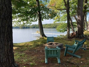 A lakeside campsite with a fire pit, two Adirondack chairs, and a view of the lake. - Camp Crocker Lakefront Home & Dock (Monmouth)