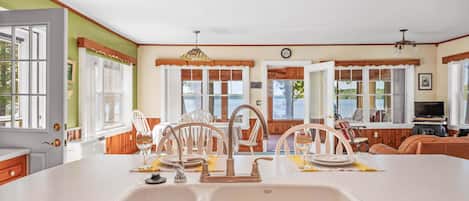 A kitchen with a large island, white cabinetry, and a view of the outdoors through the windows.