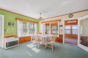 Un coin repas avec une table dressée pour quatre personnes, entouré de chaises en bois, de grandes fenêtres et offrant une vue sur l’extérieur.
