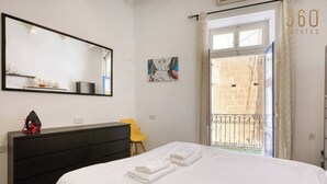 A bedroom with a bed, a dresser, a chair, a large mirror, and a view of a balcony with a railing. - Vittoriosa Townhouse 3BR – Rooftop Marina Views (Birgu)