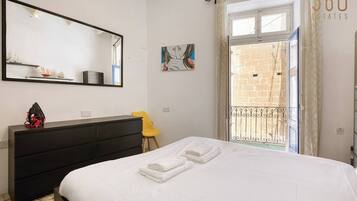 A bedroom with a bed, a dresser, a chair, a large mirror, and a view of a balcony with a railing.