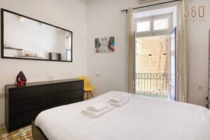 A bedroom with a bed, a dresser, a chair, a large mirror, and a view of a balcony with a railing. - Vittoriosa Townhouse 3BR – Rooftop Marina Views (Birgu)