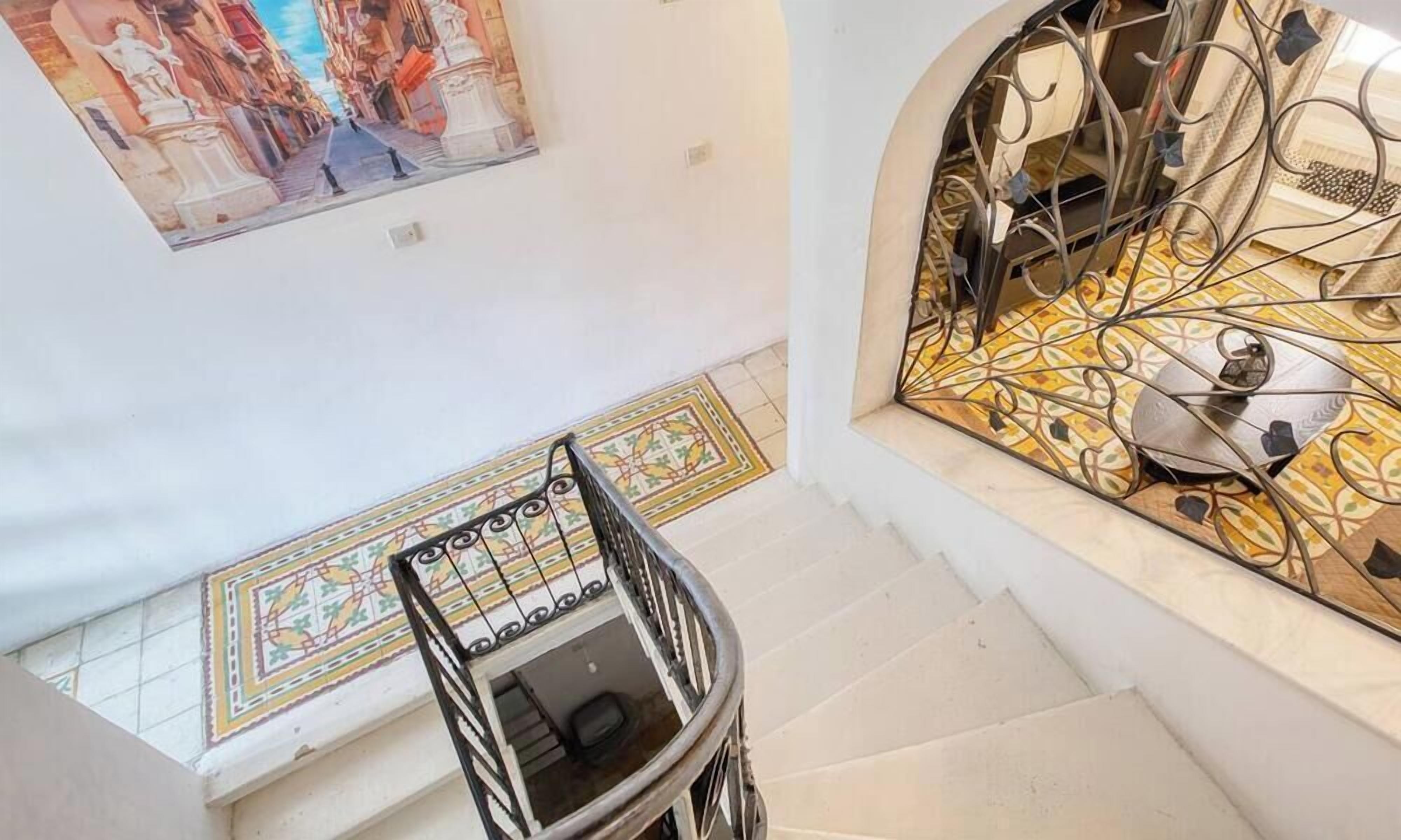Un escalier avec une rampe en métal, un sol carrelé et un mur orné d’une peinture décorative.