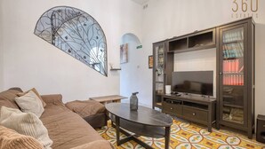A living room with a sofa, a coffee table, a TV, and a bookshelf. - Vittoriosa Townhouse 3BR – Rooftop Marina Views (Birgu)