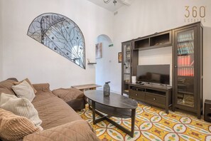 A living room with a sofa, a coffee table, a TV, and a bookshelf. - Vittoriosa Townhouse 3BR – Rooftop Marina Views (Birgu)