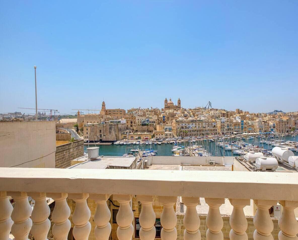 Un paisaje urbano costero con un puerto deportivo lleno de barcos, edificios históricos y cielo despejado.