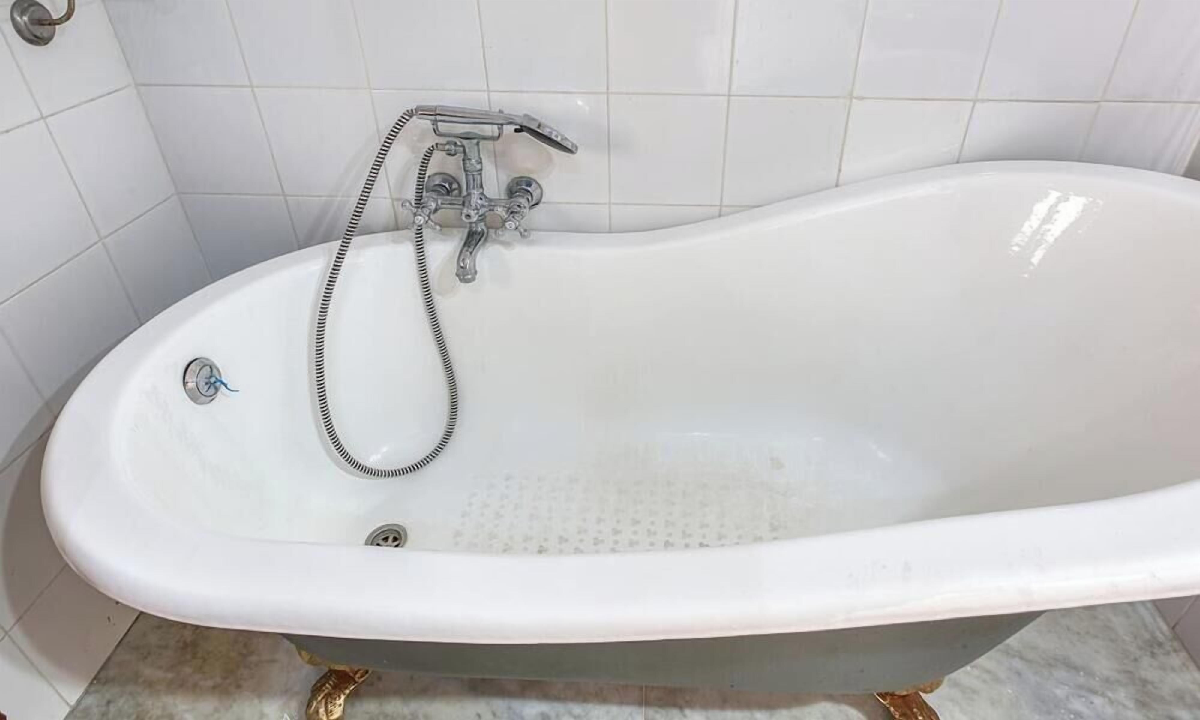 Una vasca da bagno freestanding bianca, con doccetta e flessibile, adiacente a una parete rivestita di piastrelle.