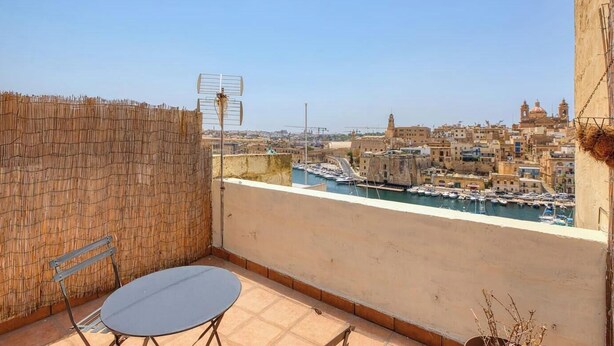 A balcony with a table and chairs, overlooking a marina with boats and a cityscape. - Vittoriosa Townhouse 3BR – Rooftop Marina Views (Birgu)