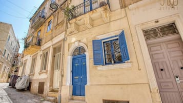 A narrow street with old buildings, a blue door, and a balcony with a wrought iron railing.