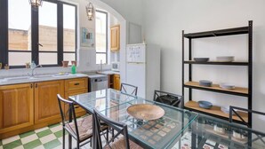 A kitchen with wooden cabinets, a glass table, and a metal shelving unit. - Vittoriosa Townhouse 3BR – Rooftop Marina Views (Birgu)