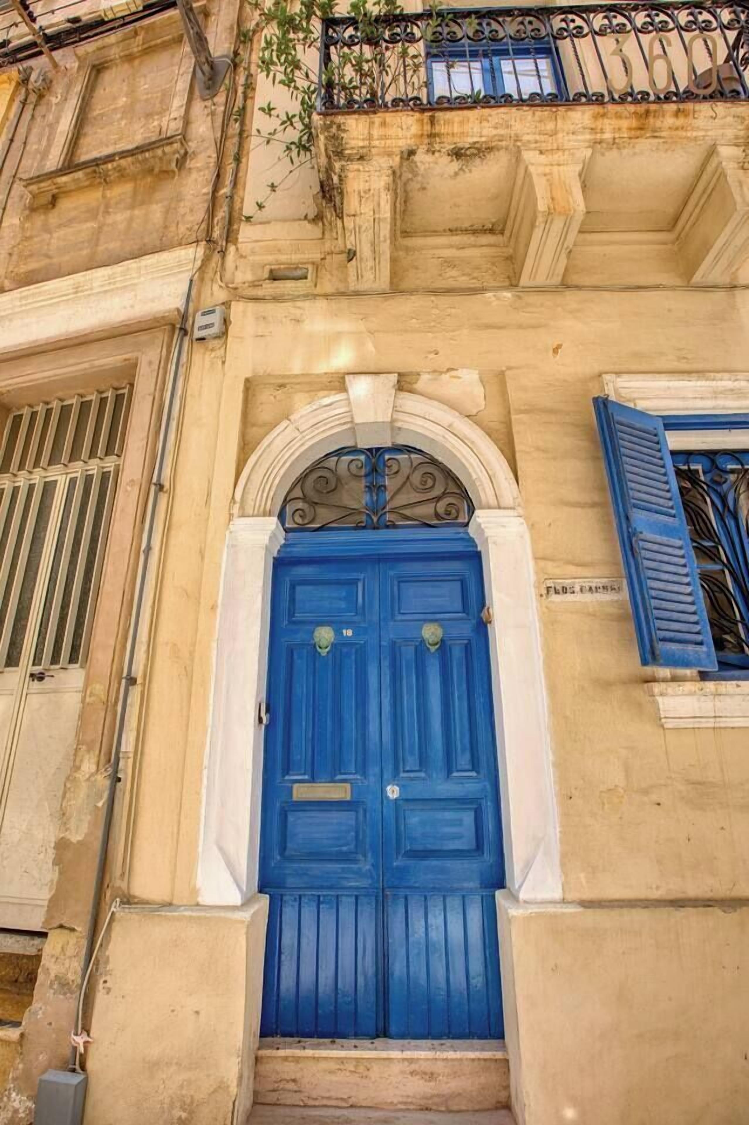 A building facade with a prominent blue door, a balcony with blue shutters, and a sign above the door.