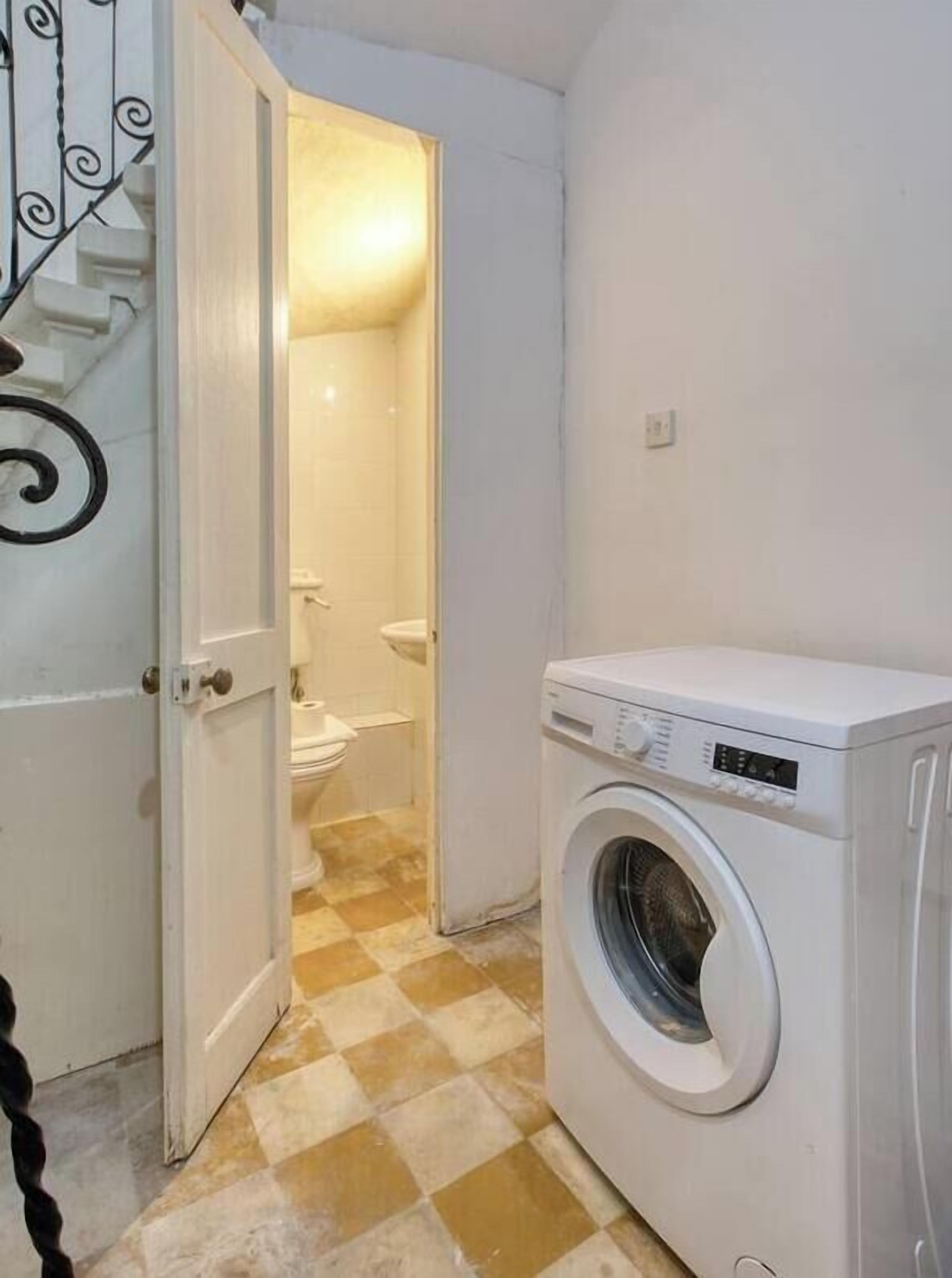 Een wasserette met een wasmachine, toilet en een geruit vloertje.