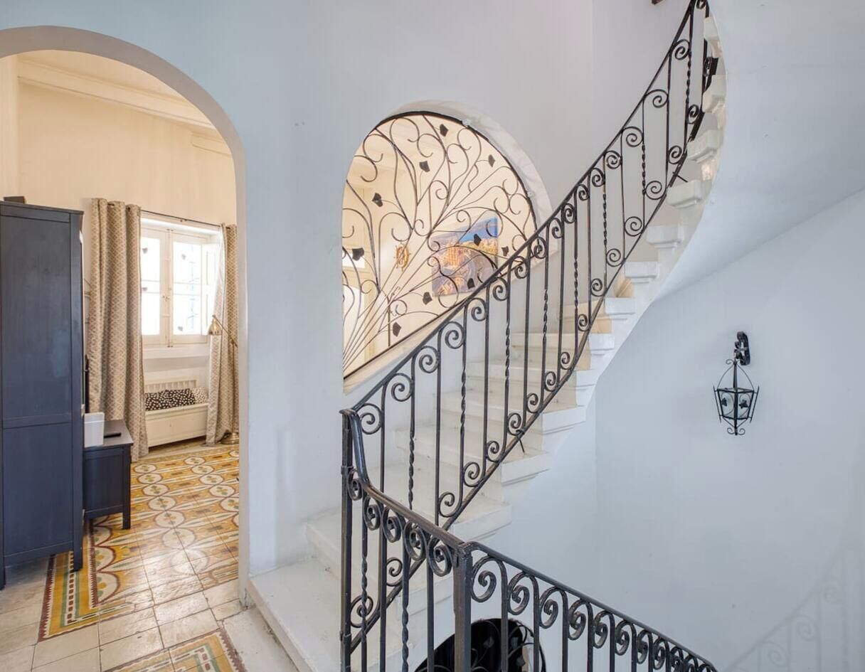 Una escalera con barandales de metal ornamentados y un ventanal con un diseño floral.