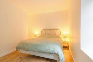 Un lit simple avec une tête de lit, deux lampes de chevet et un plancher en bois dans une pièce aux murs unis.